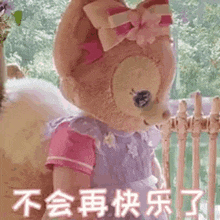 a stuffed animal with a bow on its head is standing in front of a fence .