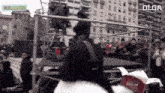 a man in a black jacket is standing in front of a crowd of people and a box that says zeballos on it .