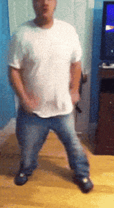 a man in a white shirt and blue jeans is dancing in front of a tv