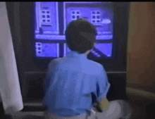 a boy in a blue shirt is standing in front of a television screen
