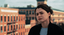 a woman stands in front of a brick building with a sad look on her face