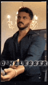 a man with a beard and mustache is standing in front of a chandelier and a sign that says o malesser