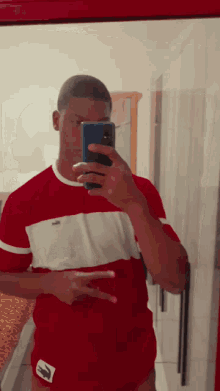 a man in a red shirt is taking a selfie in front of a mirror