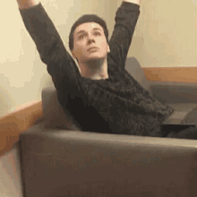 a man is sitting on a couch with his arms in the air