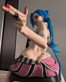 a woman with blue hair and pink nails is sitting on a chair and giving the middle finger