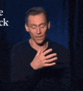 a man in a black shirt is making a gesture with his hands on a stage .