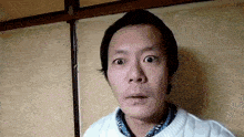 a man in a white sweater is making a funny face while standing in front of a wall .
