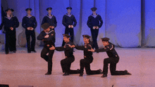 a group of men in sailor uniforms are kneeling down on a stage