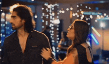 a man and a woman are standing next to each other in a room with lights hanging from the ceiling