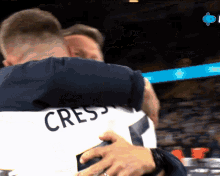 a man hugging another man with the name crest on his shirt