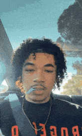 a young man with curly hair is smoking a cigarette in a car