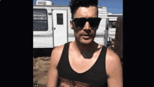 a man wearing sunglasses and a tank top is standing in front of a trailer .