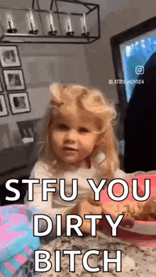 a little girl is sitting at a table eating a cookie and making a face .