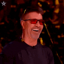 a man wearing sunglasses and a black shirt smiles for the camera