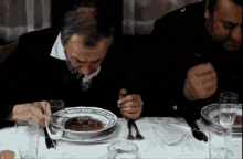 two men are sitting at a table with bowls of soup and glasses of wine