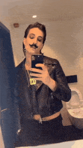 a man in a leather jacket takes a selfie in a bathroom mirror