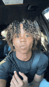 a young man with curly hair is sitting in a car with a seat belt around his neck