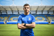 a man in a blue shirt is standing in front of a soccer field with his arms crossed .