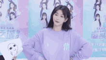 a woman wearing a purple ny sweatshirt stands in front of a wall of posters