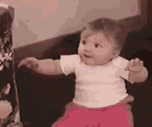 a baby girl is sitting on a couch with her arms outstretched .