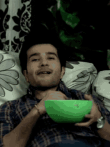 a man is laying on a couch holding a green bowl