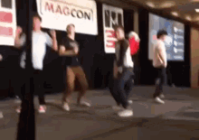a group of people are dancing on a stage in front of a sign that says magcon