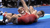 two wrestlers are wrestling on a blue mat and one has the letter l on his outfit