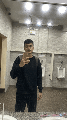 a man taking a selfie in a bathroom with urinals