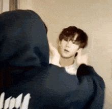 a man in a hoodie is standing in front of a mirror .