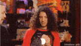 a man with long curly hair is holding a light bulb while wearing a red shirt