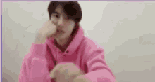 a young man wearing a pink hoodie is sitting down with his hand on his face .