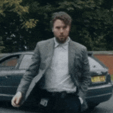 a man in a suit is standing in front of a blue car with a license plate that says jcl