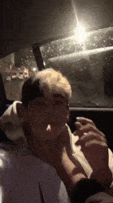 a man with blonde hair is sitting in the back seat of a car smoking a cigarette