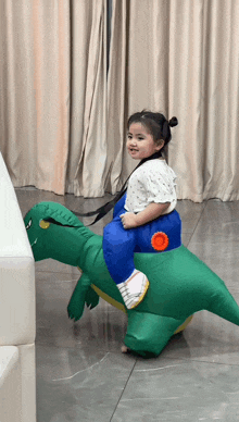 a little girl is riding a green inflatable dinosaur