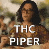 a woman wearing glasses is sitting at a table with a plate of food and the words thc piper written on it .