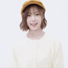 a girl wearing a yellow hat and a white sweater giving the peace sign