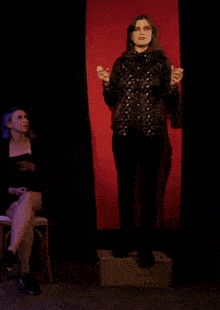a woman sitting in a chair looks at a woman standing on a stage