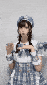 a girl in a plaid dress and hat is making a hand gesture .