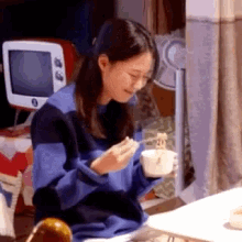 a woman is sitting at a table with a cup of coffee and a spoon in her hand .