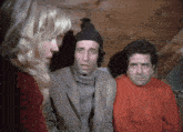 a man wearing a beanie talks to a woman and another man wearing a red sweater