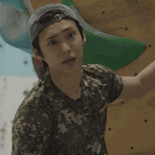 a man wearing a hat and a camouflage shirt is standing in front of a wall