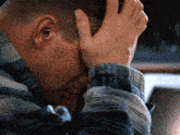 a man in a plaid shirt is covering his face with his hand
