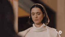 a woman wearing a white turtleneck and a white coat with a w on the bottom right