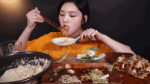 a woman in an orange shirt is eating food with chopsticks and a spoon