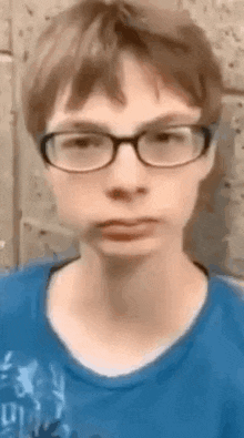 a boy wearing glasses and a blue shirt is making a funny face .