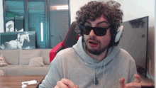 a man with curly hair wearing sunglasses and headphones is sitting in a living room .