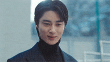 a man in a suit and black turtleneck is smiling .
