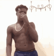 a man without a shirt is covering his nose with his hand while wearing a necklace .