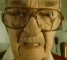 a close up of a man 's face with glasses and a mustache .