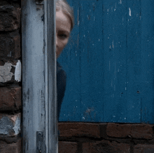 a woman is peeking out from behind a blue wooden door